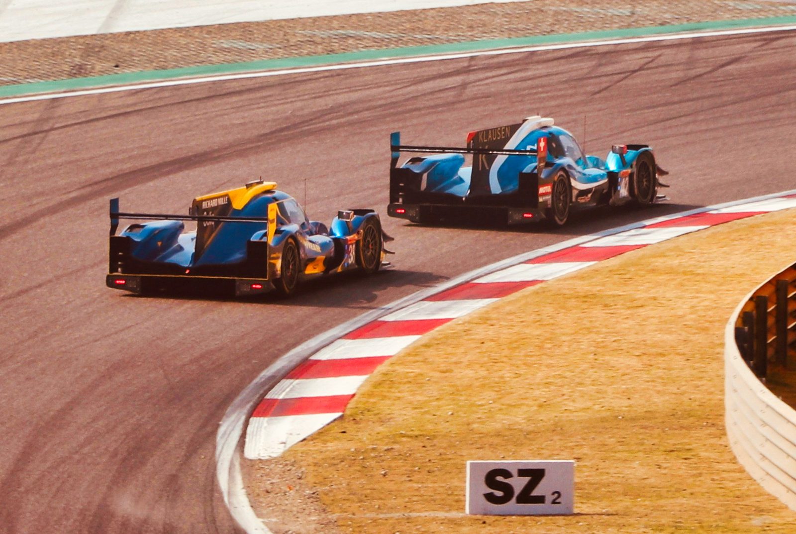 Two prototype race cars braking hard into a corner, holding the smooth line through