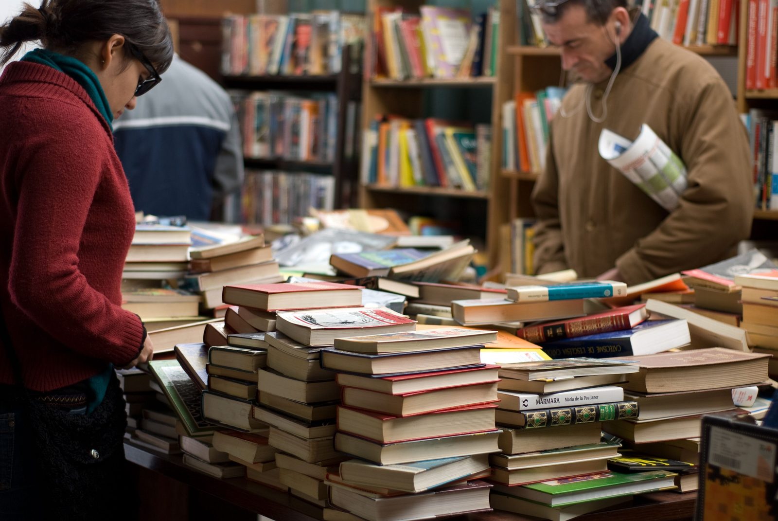 Browsers in a second-hand bookshop, each choosing a single book from tables piled with hundreds